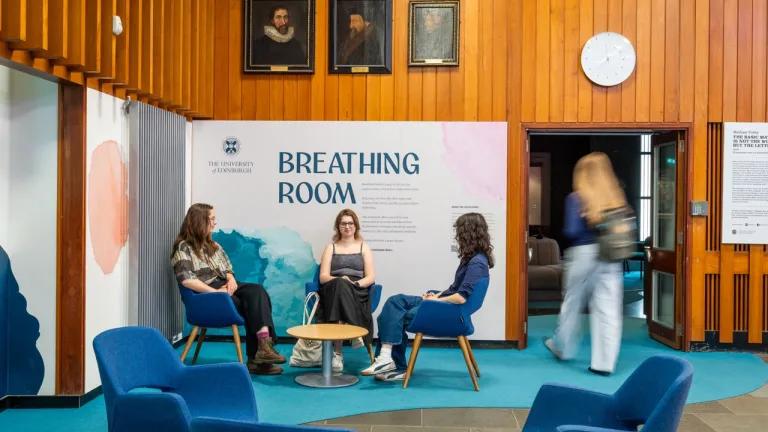 Three female students sit on chairs in front of the entrance to the gallery. A fourth female student is entering the gallery.
