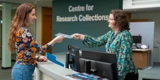 Image of the CRC helpdesk with a member of staff handing over a book to a library user