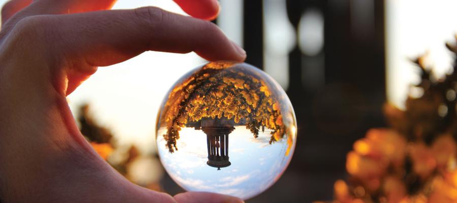 Hand in foreground holding large glass prism which shows an upside-down reflected image of Calton Hill