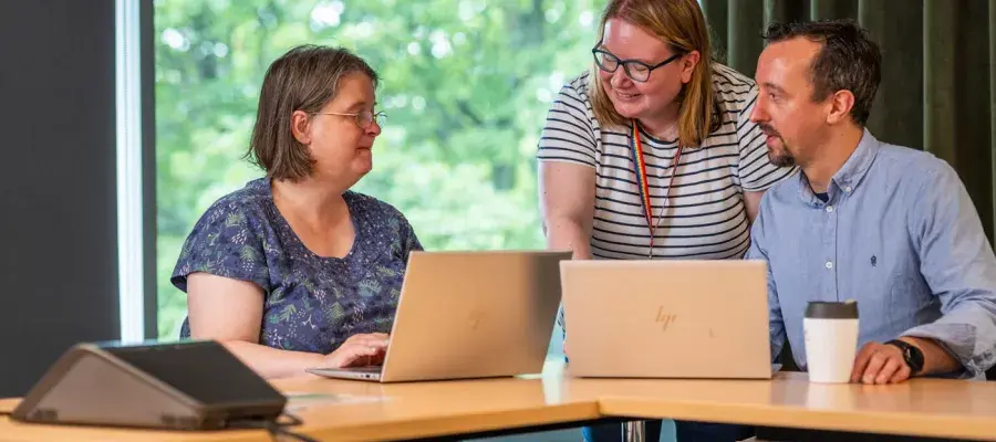 A group of people chatting at a desk with laptops