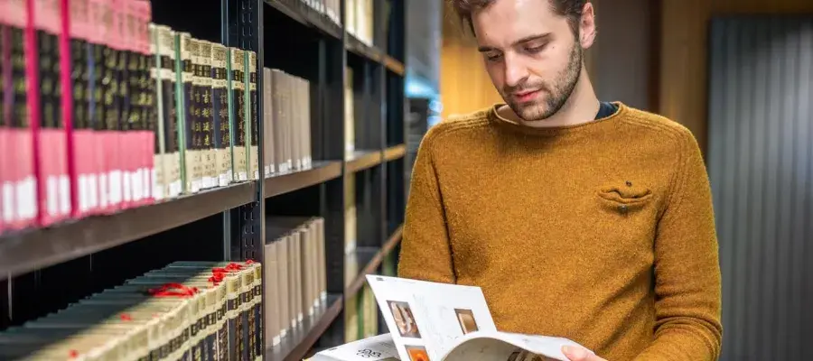 Student looking at a book off of the shelf in the Library