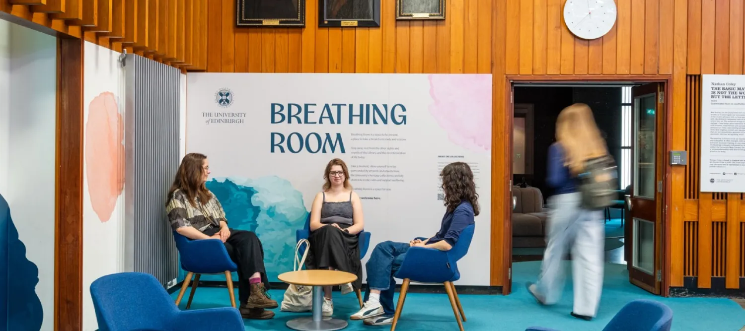 Three female students sit on chairs in front of the entrance to the gallery. A fourth female student is entering the gallery.