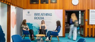Three female students sit on chairs in front of the entrance to the gallery. A fourth female student is entering the gallery.