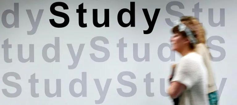 Student walking in front of a wall with the word 'Study' repeated on it