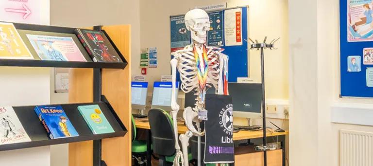 Image of a medical library with a teaching skeleton wearing a library branded bag.