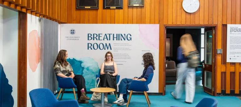 Three female students sit on chairs in front of the entrance to the gallery. A fourth female student is entering the gallery.