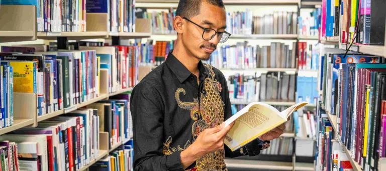 A student browsing books within the aisles of the library 