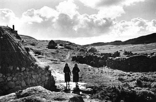 Two women walking near a blackhouse on Eriskay, 1936