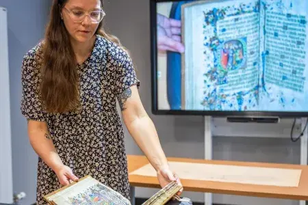 A member of staff is using an overhead camera to project an image of collections items on to a screen.