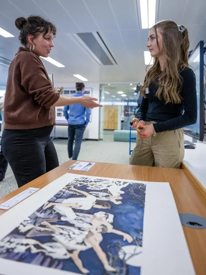 In the foreground a large artwork shows ballet dancers performing. In the background two people are in conversation about the artwork.