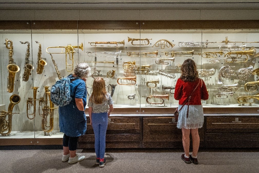 Three people looking at musical instruments in a museum