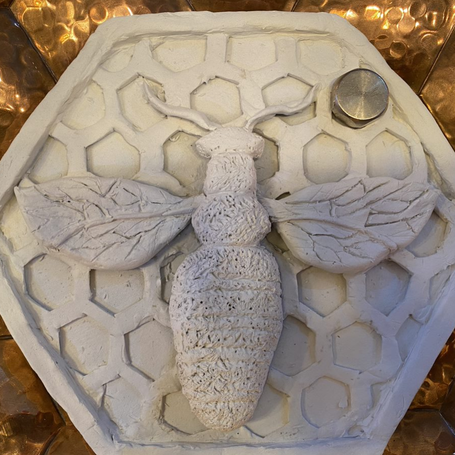 A bee tile made from clay: the background is designed to look like honeycomb with a bee on top